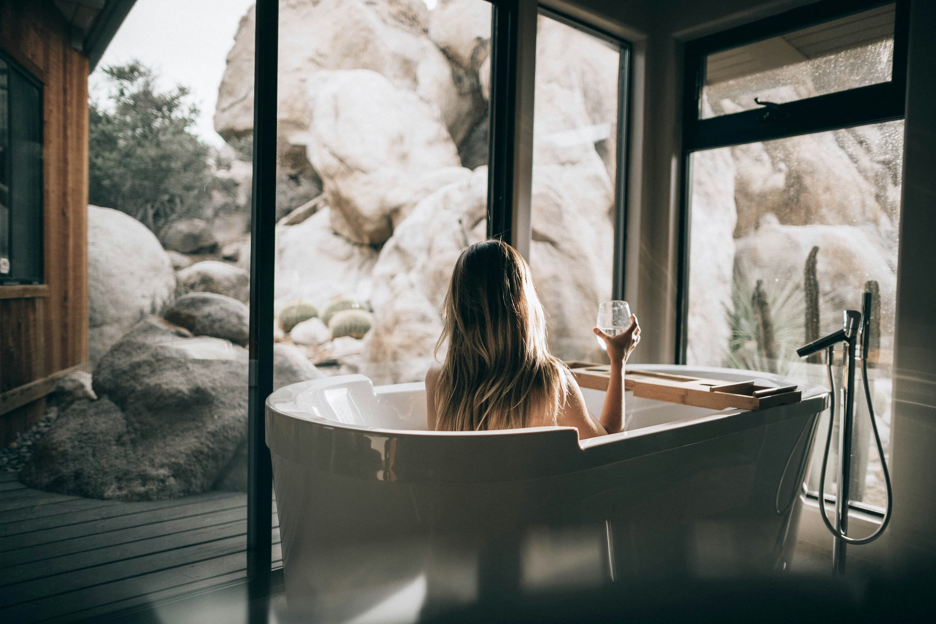 A traveler relaxing in a freestanding bathtub, gazing through floor-to-ceiling windows at a desert landscape